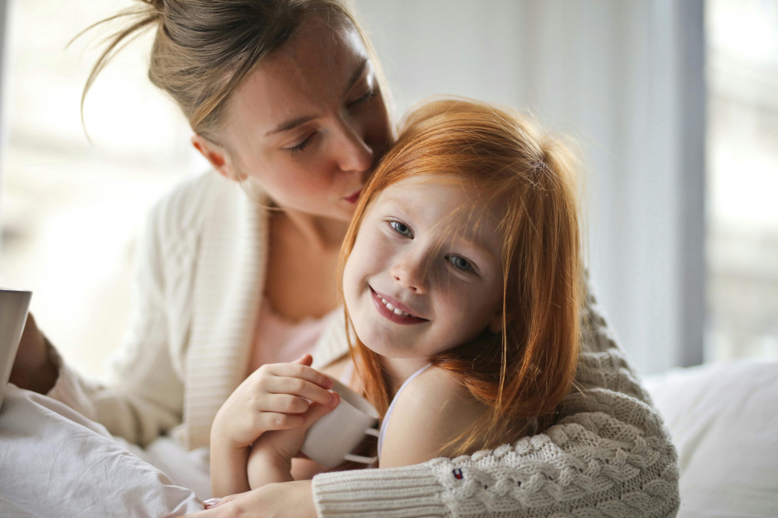 Mother kissing her smiling daughter on the head, capturing a heartwarming moment.