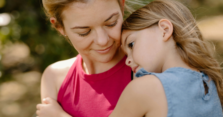 A mom in a bright pink shirt holding her daughter, who has a distant look on her face.