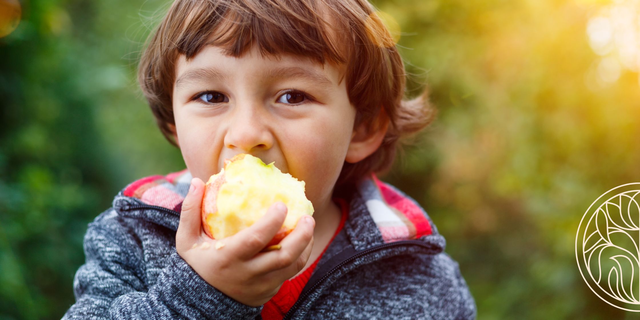 A young boy outdoors taking a bite of a fresh apple, enjoying a simple and healthy snack.