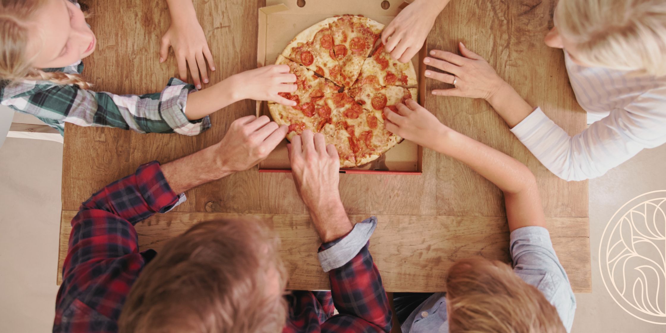 A top-down view of a pizza in an open box, with a family of four reaching in to grab slices, sharing a casual meal together.